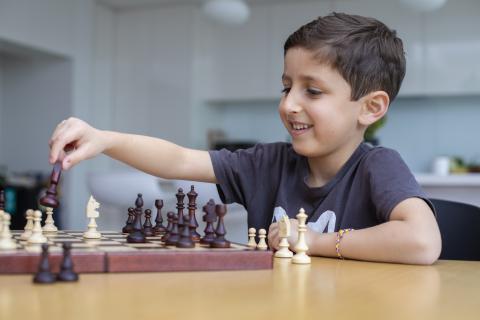 A young boy plays chess. He has a rare autoimmune condition that was diagnosed by genomic testing, enabling him to receive targeted treatment.
